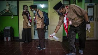 Guru SDN Kenari 07 Pagi menyemprotkan cairan disinfektan ke sepatu seorang murid sebelum memasuki ruang kelas untuk mengikuti uji coba pembelajaran tatap muka tahap dua di SD Negeri Kenari 07-08 Pagi, Jakarta, Rabu (9/6/2021). ANTARA FOTO/Aprillio Akbar
