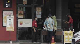 Petugas memeriksa kondisi kesehatan pengunjung sebelum memasuki gerai restoran cepat saji McDonald's Raden Saleh, Jakarta, Kamis (10/6/2021). [Suara.com/Angga Budhiyanto]