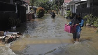 Warga berjalan melintasi banjir akibat jebolnya tanggul usai tertimpa tanah longsor di Perumahan Nerada Estate Ciputat, Tangerang Selatan, Banten, Sabtu (12/6/2021). [Suara.com/Angga Budhiyanto]