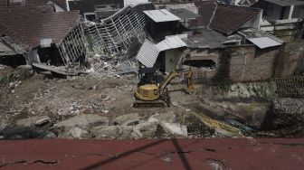 Petugas dibantu alat berat membersihkan puing-puing reruntuhan rumah yang tertimpa tanah longsor di di Perumahan Nerada Estate Ciputat, Tangerang Selatan, Banten, Sabtu (12/6/2021). [Suara.com/Angga Budhiyanto]