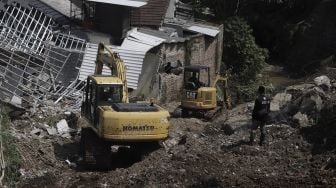 Petugas dibantu alat berat membersihkan puing-puing reruntuhan rumah yang tertimpa tanah longsor di di Perumahan Nerada Estate Ciputat, Tangerang Selatan, Banten, Sabtu (12/6/2021). [Suara.com/Angga Budhiyanto]