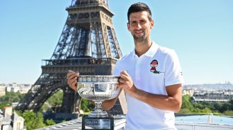 Petenis tunggal putera Serbia Novak Djokovic berpose dengan piala kemenangannya di depan Menara Eiffel, di Paris, Prancis, Senin (14/6 /2021).  Christophe ARCHAMBAULT / POOL / AFP