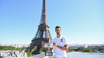 Petenis tunggal putera Serbia Novak Djokovic berpose dengan piala kemenangannya di depan Menara Eiffel, di Paris, Prancis, Senin (14/6 /2021).  Christophe ARCHAMBAULT / POOL / AFP