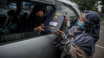 Seorang guru memberikan rapor kepada orang tua siswa saat penerimaan rapor dengan layanan tanpa turun di SD Darul Hikam, Bandung, Jawa Barat, Selasa (15/6/2021).  ANTARA FOTO/Raisan Al Farisi