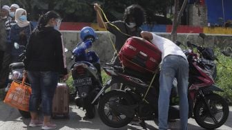 Pekerja Migran Indonesia (PMI) menaikkan barang bawaan ke atas motor usai menjalani isolasi di Rumah Sakit Darurat COVID-19 (RSDC) Wisma Atlet Pademangan, Jakarta, Selasa (15/6/2021). [Suara.com/Angga Budhiyanto]