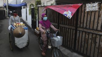 Pedagang jamu keliling melintas di zona merah COVID-19 RT 006 RW 01, Gandaria Selatan, Cilandak, Jakarta, Selasa (22/6/2021). [Suara.com/Angga Budhiyanto]