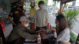 Petugas Satpol PP Kabupaten Badung memberikan sanksi administrasi berupa denda Rp100 ribu kepada warga negara asing (WNA) yang melanggar protokol kesehatan saat operasi penertiban prokes dalam Pemberlakuan Pembatasan Kegiatan Masyarakat (PPKM) skala mikro di Desa Canggu, Badung, Bali, Jumat (25/6/2021).  ANTARA FOTO/Nyoman Hendra Wibowo
