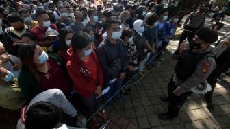 Anggota Polisi mengarahkan ribuan warga yang antre vaksinasi COVID-19 massal di Denpasar, Bali, Sabtu (26/6/2021). FOTO/Nyoman Hendra Wibowo