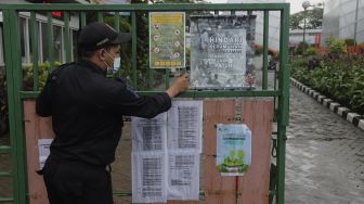 Petugas keamanan menutup pintu masuk Tempat Pemakaman Umum (TPU) Karet Bivak, Jakarta, Minggu (27/6/2021). [Suara.com/Angga Budhiyanto]