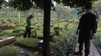 Petugas membersihkan makam di Tempat Pemakaman Umum (TPU) Karet Bivak, Jakarta, Minggu (27/6/2021). [Suara.com/Angga Budhiyanto]