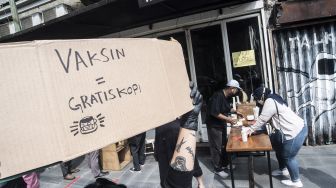 Seorang barista membawa papan pengumuman pembagian kopi gratis bagi masyarakat yang sudah vaksin COVID-19 di kawasan Blok M, Jakarta, Rabu (30/6/2021). ANTARA FOTO/Muhammad Adimaja