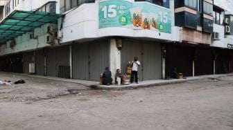 Pedagang asongan beristirahat di pelataran toko yang tutup di Pasar Tanah Abang, Jakarta Pusat, Sabtu (3/7/2021). [Suara.com/Alfian Winanto]