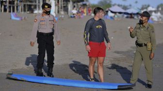 Petugas Satpol PP dan Polisi meminta wisatawan untuk meninggalkan objek wisata pantai yang ditutup saat melakukan pengawasan Pemberlakuan Pembatasan Kegiatan Masyarakat (PPKM) Darurat di kawasan Canggu, Badung, Bali, Minggu (4/7/2021). [ANTARA FOTO/Fikri Yusuf]