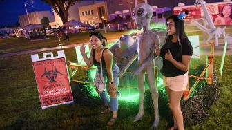 Orang-orang berfoto dengan patung alien selama Festival UFO di Roswell, New Mexico, pada (2/7/2021). [Patrick T. FALLON / AFP]