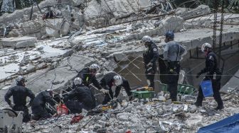 Personel pencarian dan penyelamatan melanjutkan bekerja di tengah hujan di tumpukan puing-puing kondominium Champlain Towers South yang sebagian runtuh di Surfside, Florida, pada (5/7/2021). [Giorgio Viera / AFP]