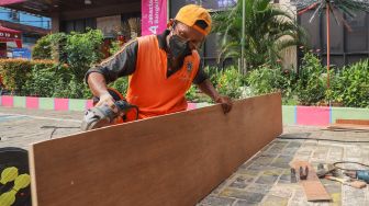 Petugas memotong kayu saat pembuatan peti mati di Kantor Kelurahan Kayu Putih, Jakarta Timur, Selasa (6/7/2021). [Suara.com/Alfian Winanto]