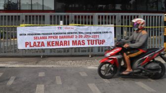 Warga melintas di depan spanduk berisi informasi penutupan Plaza Kenari Mas di kawasan Senen, Jakarta Pusat, Kamis (8/7/2021). [Suara.com/Alfian Winanto]