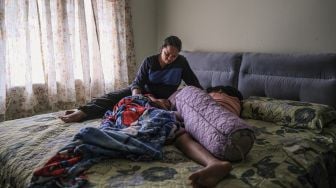 Seorang janda, Tilda Kalaivani duduk di samping kedua anaknya saat mereka tidur di apartemen sewaannya di Kuala Lumpur, Malaysia, pada (6/7/2021). [Mohd RASFAN / AFP]