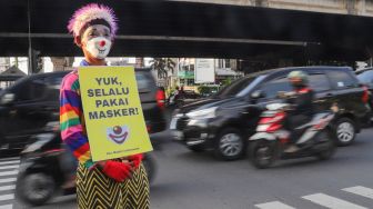 Angggota Komunitas Aku Badut Indonesia (ABI) membawa poster berisi ajakan untuk menggunakan masker di kawasan Cilandak, Jakarta Selatan, Senin (12/7/2021). [Suara.com/Alfian Winanto]