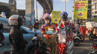 Angggota Komunitas Aku Badut Indonesia (ABI) membagi-bagikan masker kepada pengendara motor saat melakukan aksi kampanye untuk menggunakan masker di kawasan Cilandak, Jakarta Selatan, Senin (12/7/2021). [Suara.com/Alfian Winanto]