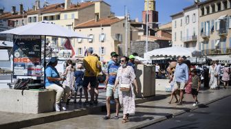 Turis dan penduduk lokal berjalan melewati pelabuhan tua setelah Prancis baru-baru ini melonggarkan tindakan pencegahan penyebaran COVID-19 di Ramatuelle, Saint-Tropez, Prancis, pada (10/7/2021). [CLEMENT MAHOUDEAU / AFP]