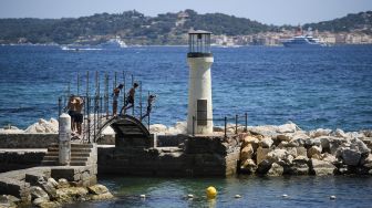 Orang-orang melompat dari jembatan di pantai Les Cigales di Port-Grimaud, dengan latar belakang Saint-Tropez, Prancis, pada (10/7/2021). [CLEMENT MAHOUDEAU / AFP]