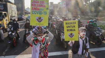 Angggota Komunitas Aku Badut Indonesia (ABI) membawa poster berisi ajakan untuk menggunakan masker di kawasan Cilandak, Jakarta Selatan, Senin (12/7/2021). [Suara.com/Alfian Winanto]