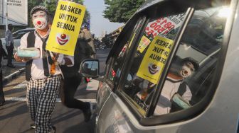 Angggota Komunitas Aku Badut Indonesia (ABI) membagi-bagikan masker kepada pengendara motor saat melakukan aksi kampanye untuk menggunakan masker di kawasan Cilandak, Jakarta Selatan, Senin (12/7/2021). [Suara.com/Alfian Winanto]