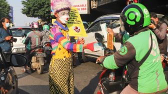 Angggota Komunitas Aku Badut Indonesia (ABI) membagi-bagikan masker kepada pengendara motor saat melakukan aksi kampanye untuk menggunakan masker di kawasan Cilandak, Jakarta Selatan, Senin (12/7/2021). [Suara.com/Alfian Winanto]