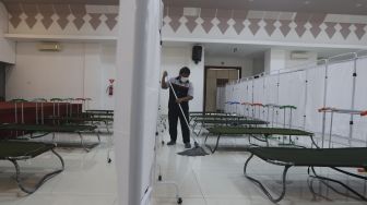 Petugas membersihkan ruangan yang akan dijadikan tempat isolasi mandiri di GOR Kecamatan Matraman, Jakarta, Selasa (13/7/2021). [Suara.com/Angga Budhiyanto]