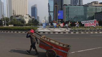 Seorang warga berjalan di dekat maskot dan slogan Pekan Olahraga Nasional (PON) XX Papua di Bundaran Hotel Indonesia, Jakarta, Jumat (16/7/2021). [Suara.com/Angga Budhiyanto]