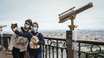 Pengunjung berswafoto dari lantai dua Menara Eiffel di Paris, Prancis, pada (16/7/2021). [Bertrand GUAY / AFP]