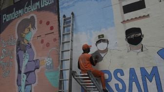 Pekerja Penanganan Sarana dan Prasarana Umum (PPSU) menyelesaikan mural melawan COVID-19 di tembok di kawasan Cikokol, Cawang, Jakarta, Jumat (23/7/2021). [Suara.com/Angga Budhiyanto]