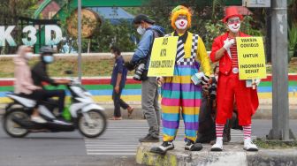 Angggota Komunitas Aku Badut Indonesia (ABI) melakukan aksi kampanye untuk mengajak masyarakat melakukan vaksinasi dan mematuhi protokol kesehatan di Kawasan Juanda, Depok, Jawa Barat, Jumat (23/7/2021). [Suara.com/Alfian Winanto]