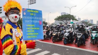 Poster berisi ajakan masyarakat melakukan vaksinasi dan mematuhi protokol kesehatan ditunjukkan oleh anggota komunitas Aku Badut Indonesia (ABI) saat menggelar aksi kampanye di Kawasan Juanda, Depok, Jawa Barat, Jumat (23/7/2021). [Suara.com/Alfian Winanto]