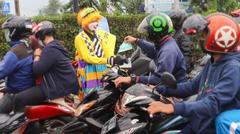 Angggota Komunitas Aku Badut Indonesia (ABI) membagikan masker kepada pengendara motor saat melakukan aksi kampanye untuk mengajak masyarakat melakukan vaksinasi dan mematuhi protokol kesehatan di Kawasan Juanda, Depok, Jawa Barat, Jumat (23/7/2021). [Suara.com/Alfian Winanto]