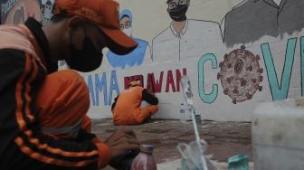 Pekerja Penanganan Sarana dan Prasarana Umum (PPSU) menyelesaikan mural melawan COVID-19 di tembok di kawasan Cikokol, Cawang, Jakarta, Jumat (23/7/2021). [Suara.com/Angga Budhiyanto]