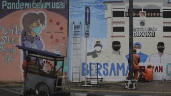 Pekerja Penanganan Sarana dan Prasarana Umum (PPSU) menyelesaikan mural melawan COVID-19 di tembok di kawasan Cikokol, Cawang, Jakarta, Jumat (23/7/2021). [Suara.com/Angga Budhiyanto]