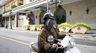 Seorang warga mengenakan masker dan pelindung wajah mengendarai skuternya di sepanjang jalan yang hampir kosong di Hanoi, Vietnam, Sabtu (24/7/2021). [Manan VATSYAYANA / AFP]