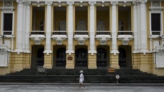 Seorang warga mengenakan masker berjalan melewati Gedung Opera di Hanoi, Vietnam, Sabtu (24/7/2021). [Manan VATSYAYANA / AFP]