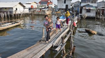 Warga berjalan di atas jembatan kayu di perkampungan nelayan Muara Angke, Jakarta Utara, Sabtu (31/7/2021). ANTARA FOTO/Indrianto Eko Suwarso