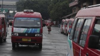 Seorang calon penumpang berjalan di dekat deretan angkutan umum kota (angkot) di Terminal Kampung Rambutan, Jakarta, Kamis (5/8/2021). [Suara.com/Angga Budhiyanto]