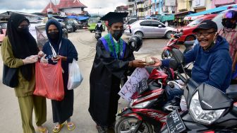 Seorang mahasiswa yang baru selesai wisuda (tengah) bersama komunitas Maluku membagikan nasi bungkus kepada warga di Pasar Batu Merah, Kota Ambon, Provinsi Maluku, Kamis (5/8/2021). ANTARA FOTO