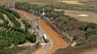 Sebuah kendaraan pertanian melaju di jalan tanah kota Israel Metula di sepanjang pagar perbatasan antara kedua negara, di Marjayoun, Lebanon, pada (6/8/2021). [Mahmoud ZAYYAT / AFP]