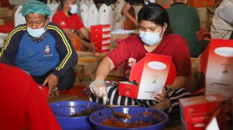 Petugas mengemas makanan ke dalam box di dapur umum Kementerian Sosial di Gedung Konvensi, Taman Makam Pahlawan (TMP) Kalibata, Jakarta, Minggu (8/8/2021). [Suara.com/Alfian Winanto]