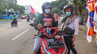 Warga menunjukkan pernak pernik bendera merah putih yang dibelinya di Jalan Matraman Raya, Jatinegara, Jakarta Timur, Minggu (8/8/2021). [Suara.com/Alfian Winanto]