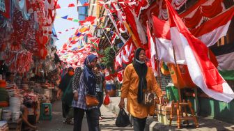 Warga melintas di area pasar yang dipenuhi ornamen dan pernak-pernik bendera merah putih di Pasar Jatinegara, Jakarta Timur, Rabu (11/8/2021). [Suara.com/Alfian Winanto]