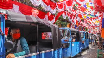 Transportasi Bajai melintasi area pasar yang dipenuhi ornamen dan pernak-pernik bendera merah putih di Pasar Jatinegara, Jakarta Timur, Rabu (11/8/2021). [Suara.com/Alfian Winanto]