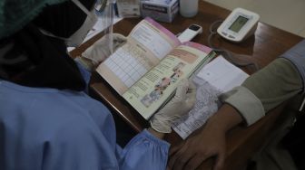 Petugas kesehatan memeriksa buku kesehatan ibu dan anak sebelum memberikan vaksinasi COVID-19 di Gedung Wira Purusa LVRI DKI Jakarta, Kamis (12/8/2021). [Suara.com/Angga Budhiyanto]