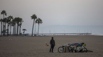 Seorang tunawisma berdiri di depan tendanya pada pagi hari di Pantai Venesia, California, Amerika Serikat, pada (12/8/2021). [Apu GOMES / AFP]